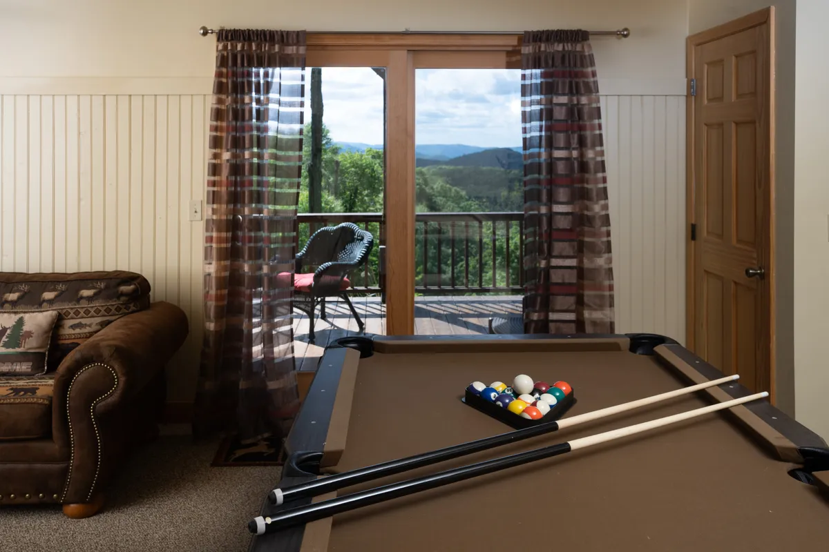 A casual recreation space featuring a pool table next to curtains and a window that offers glimpses of the scenic views outside. The setup encourages intimate game nights and relaxed social interactions, all within sight of the surrounding natural beauty.