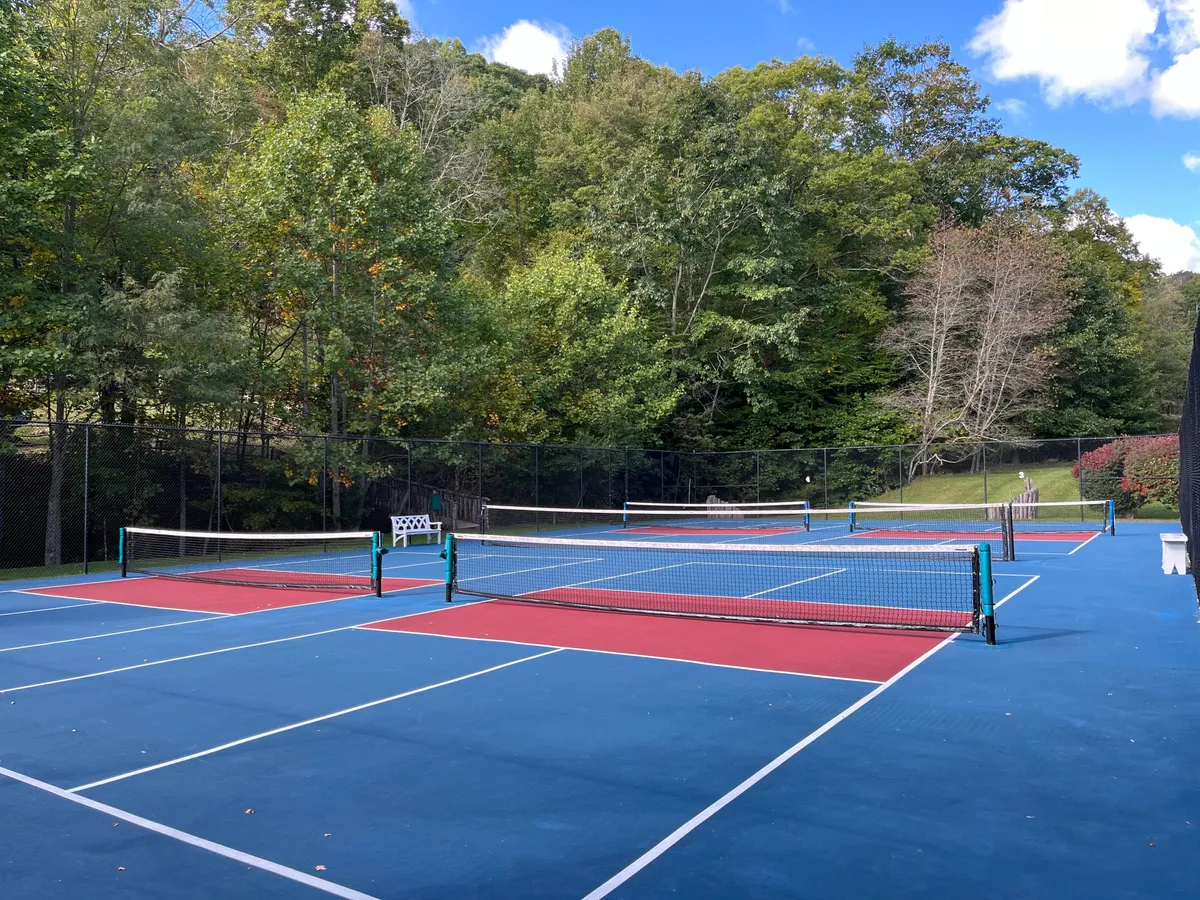 Sun-drenched tennis courts set amid lush greenery, with benches for spectating and relaxation. The well-maintained courts evoke fun afternoons of active play and family bonding, all surrounded by the natural beauty of the mountains.
