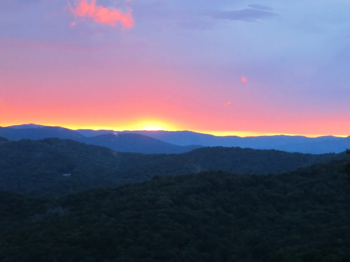 A wide, panoramic view of distant mountain ridges set aglow by the colors of sunset. The scene is tranquil and imbued with a sense of peaceful solitude, inviting relaxation and contemplation.