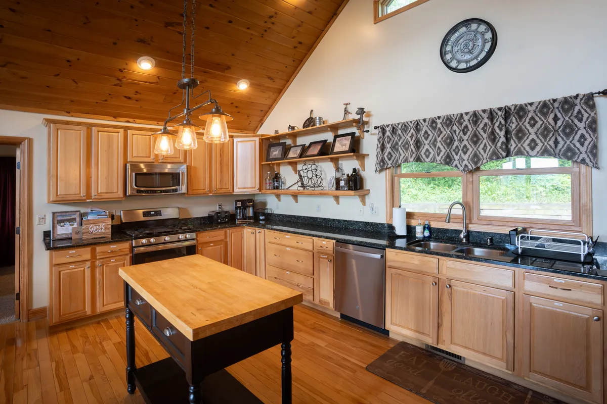 A stylish kitchen featuring an island countertop, modern stainless steel appliances, ample wooden cabinetry, and decorative shelves. The layout and finish indicate a space designed for group cooking, holiday meals, and celebratory gatherings.