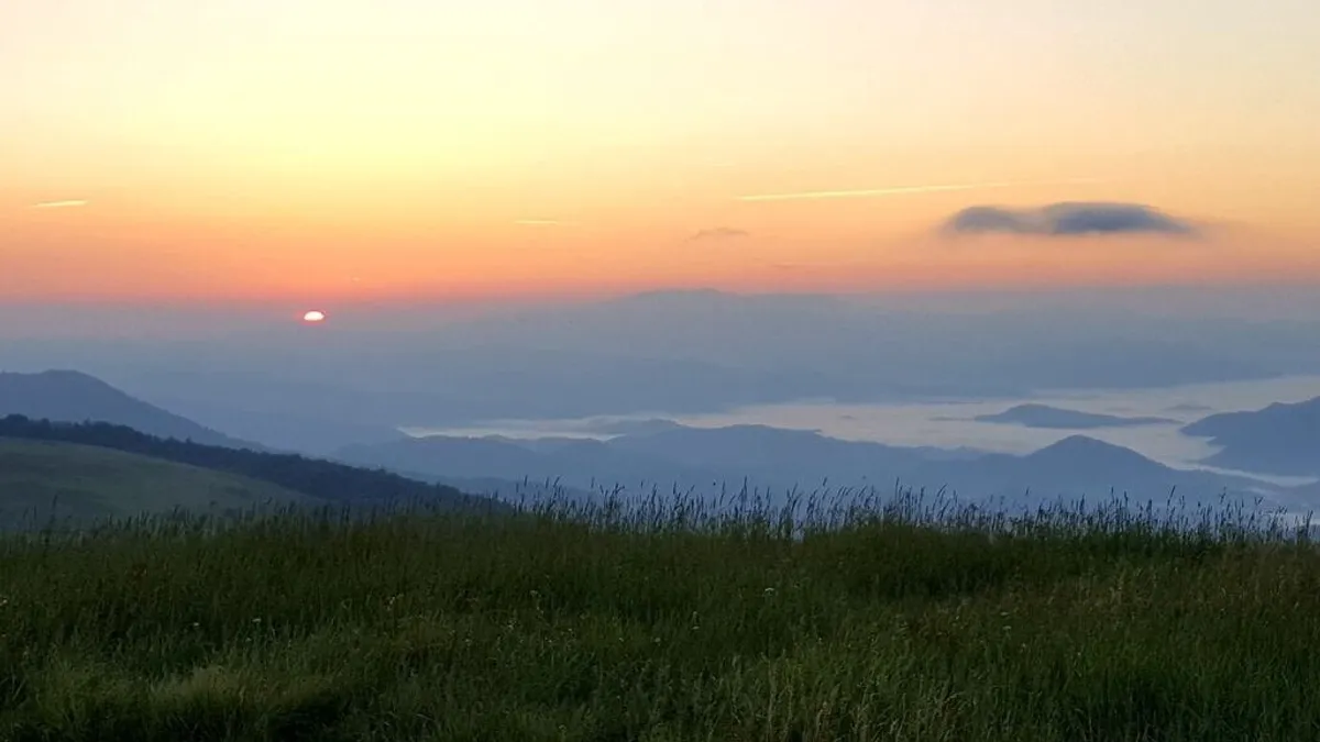 A panoramic view of a breathtaking sunset over a mountain range, with colorful clouds and expansive sky. The vista invokes a sense of serenity and awe, highlighting the beauty of the surrounding landscape that the deck overlooks.